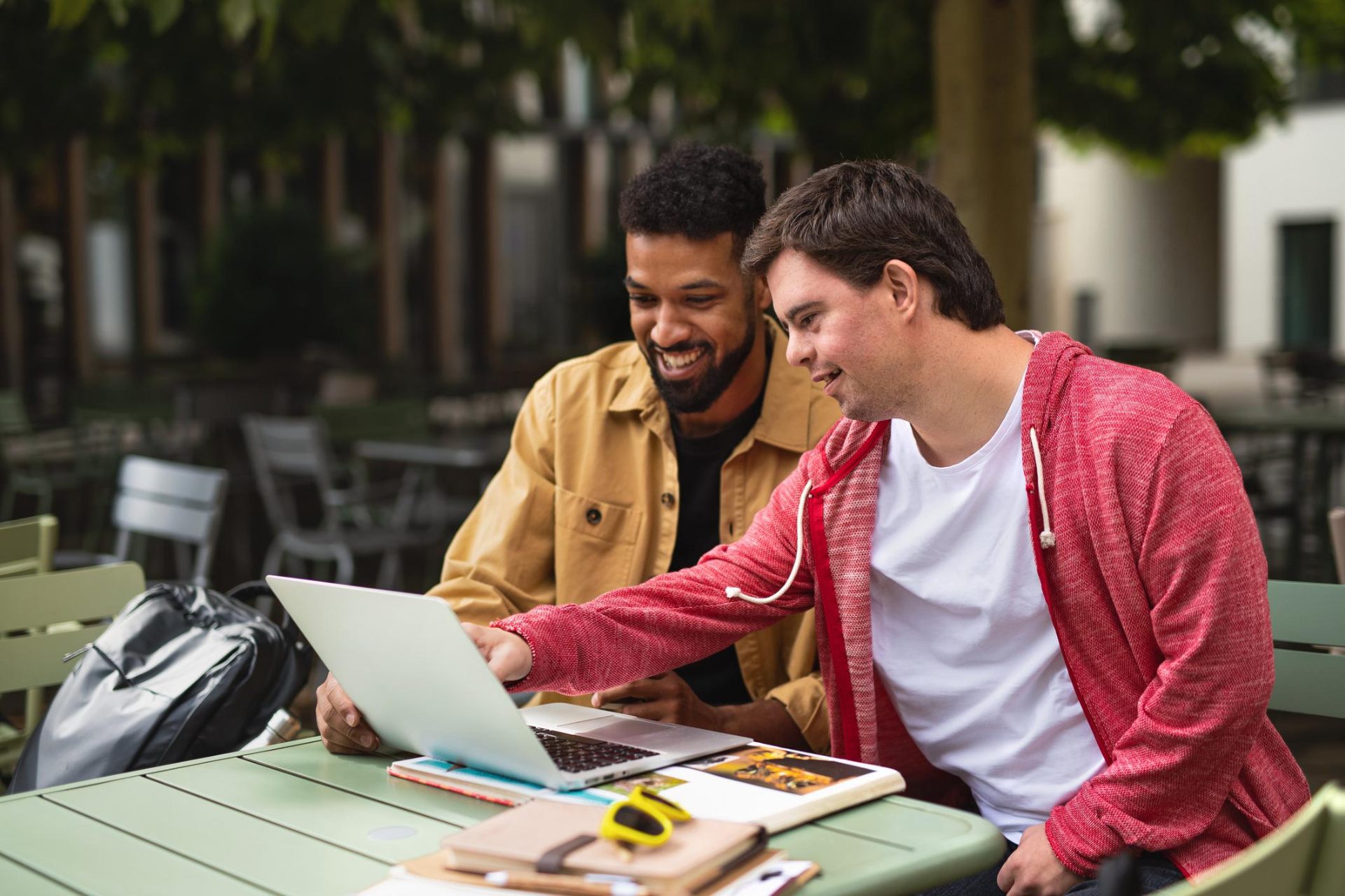 Two young men working together on a laptop at an outdoor cafe